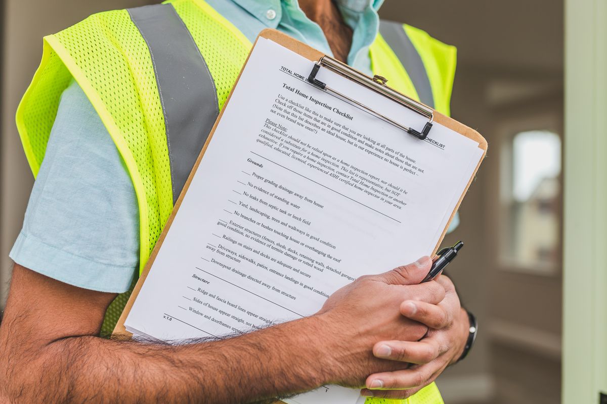Inspector in safety vest holding a clipboard with a detailed building inspection checklist