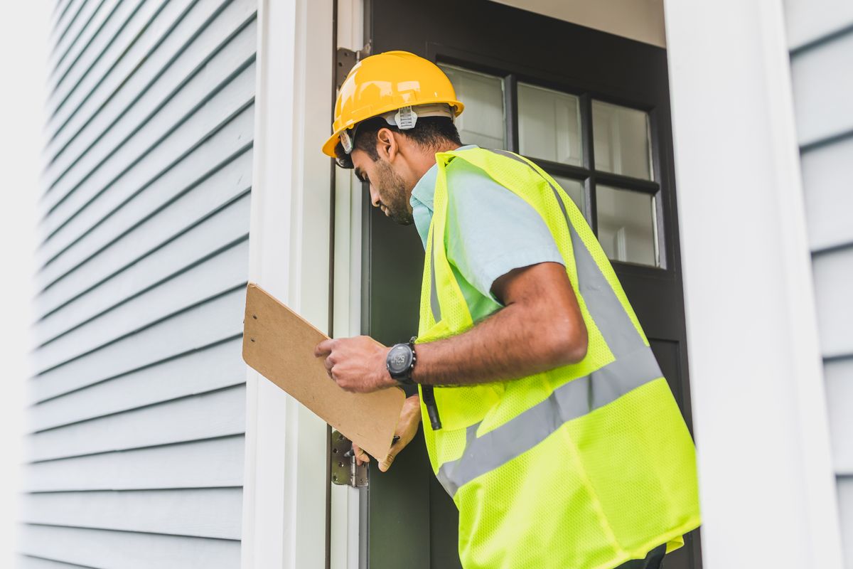 Inspector with clipboard examining the exterior doorway and siding of an older building